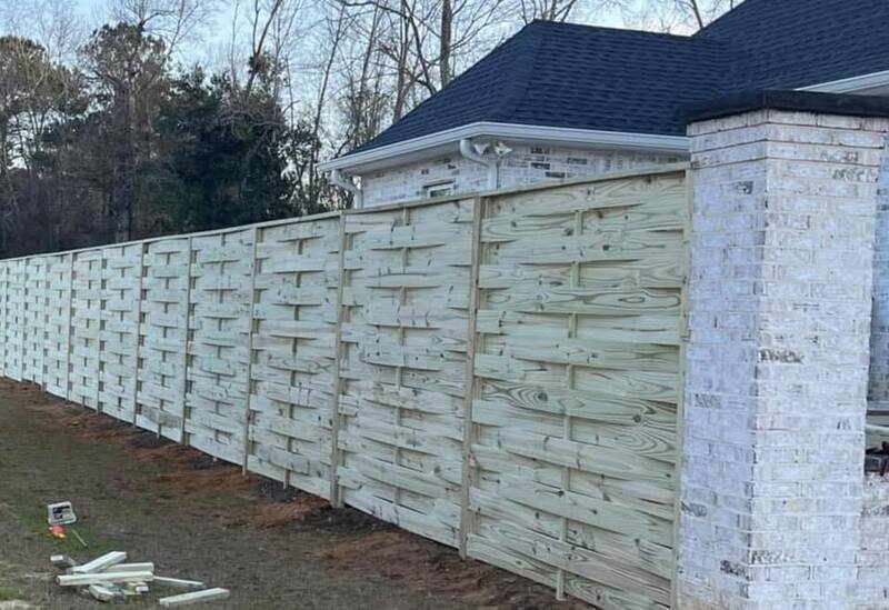 Tall basket-weave wood fence between whitewashed brick columns at a house