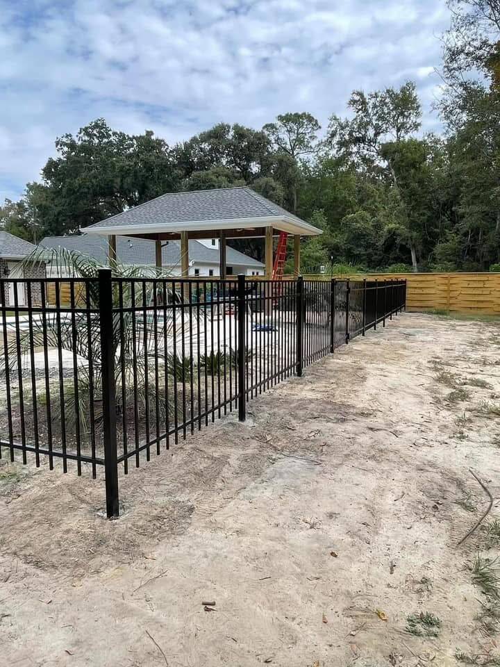 Black metal picket fence on new posts across a sandy yard