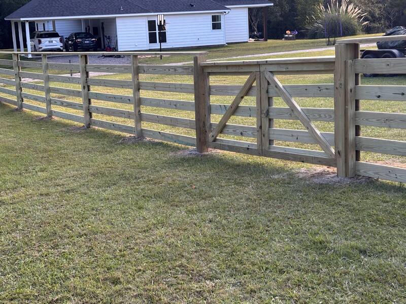 Four-board wood ranch fence with a wide X-braced wood gate on an open lawn
