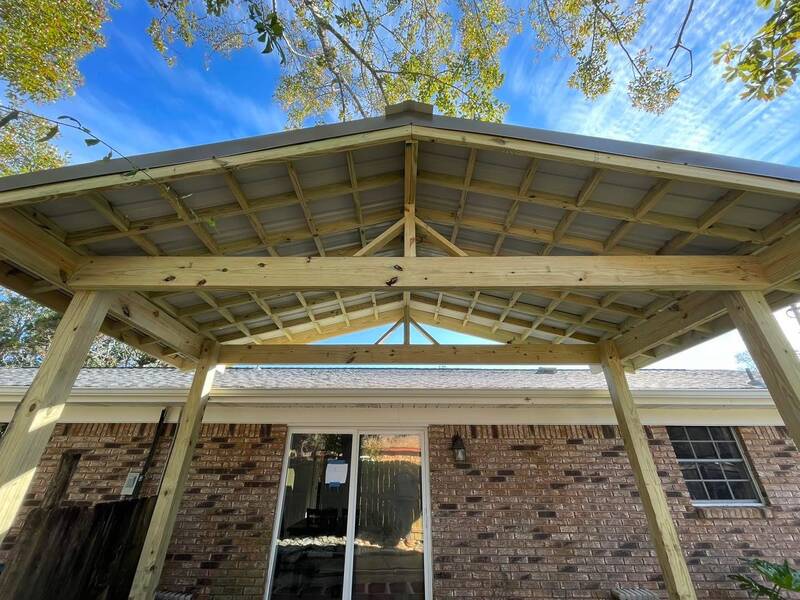 Looking up into the gable roof framing of a new wood patio cover attached to a brick house